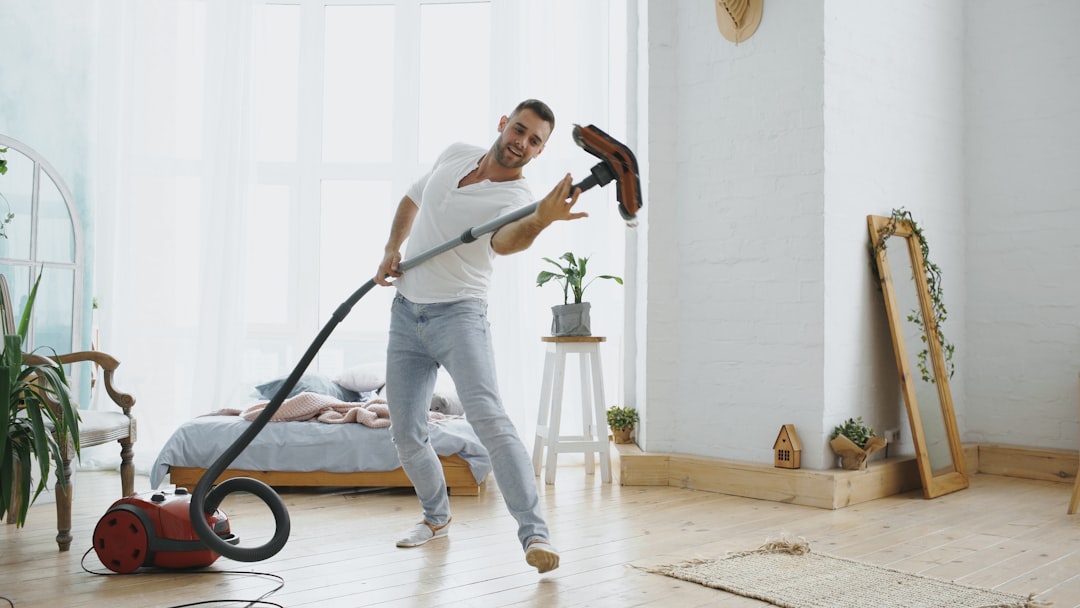 Dancing young man having fun cleaning house with vacuum cleaner at home